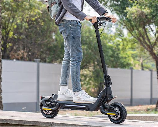A young man wearing a helmet is riding a Todimart-X5s electric scooter: a black Todimart-X5s electric scooter (equipped with durable tires) – casual attire, outdoor setting – perfect for city commuting
