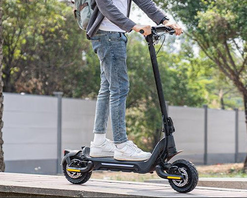 A young man wearing a helmet is riding a Todimart-X5s electric scooter: a black Todimart-X5s electric scooter (equipped with durable tires) – casual attire, outdoor setting – perfect for city commuting